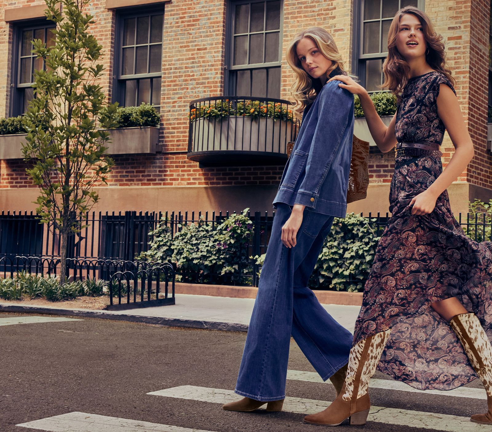 Two models crossing a street, one wearing the cow print and suede Wyatt knee high boot styled with a long paisley dress.