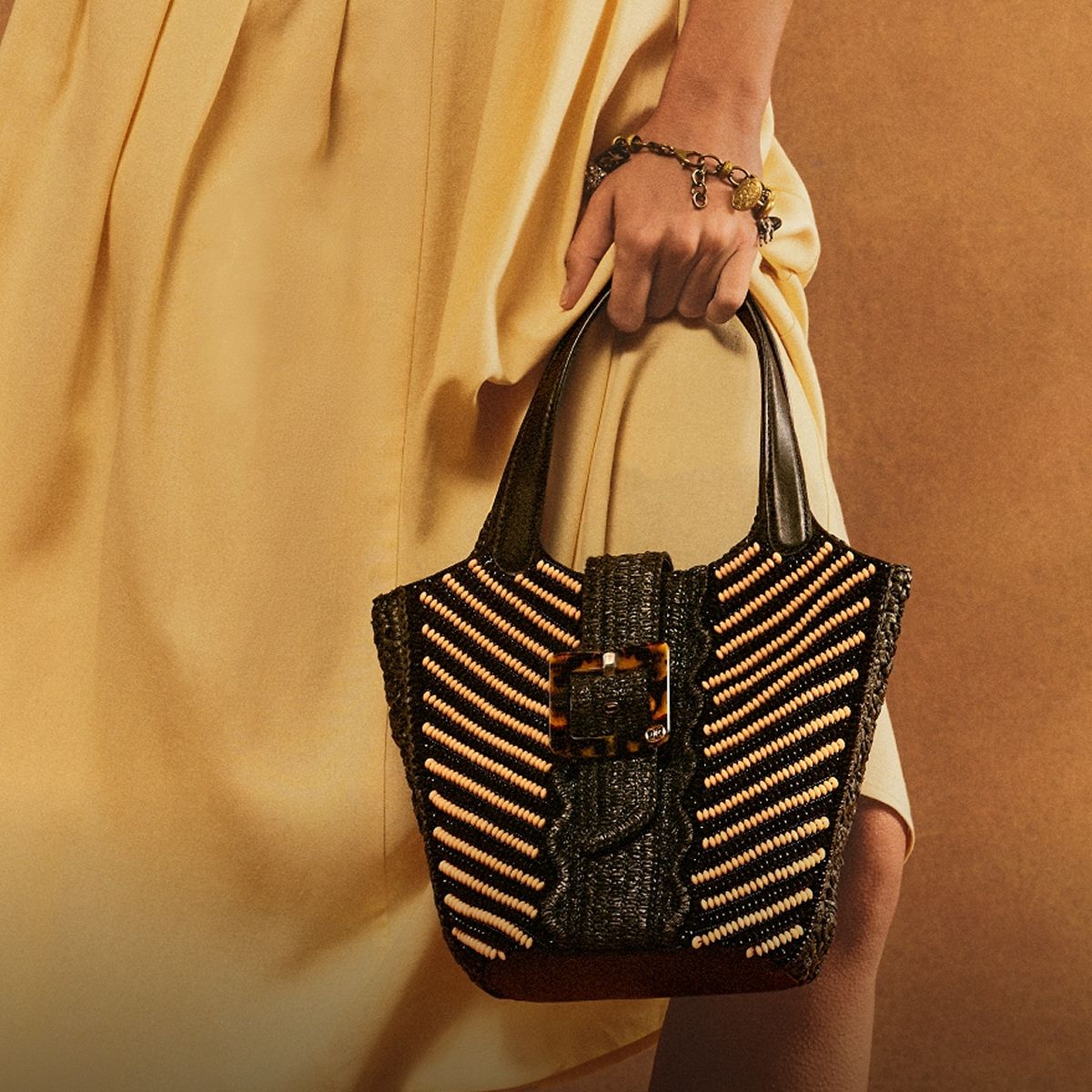 Model holding a black Sam Edelman woven top handle bag with diagonal beads and a tortoiseshell buckle.