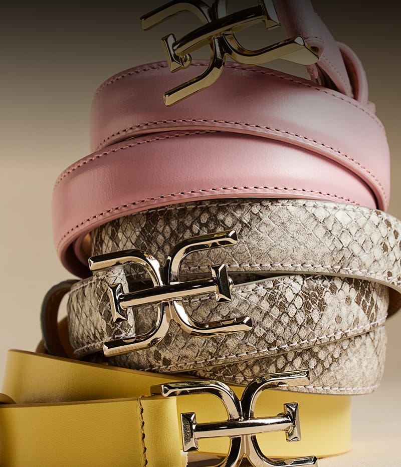 Stack of three Sam Edelman leather belts with gold double E logo buckles in pink, snakeskin, and yellow.
